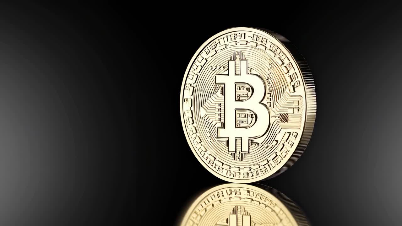 A close-up video still of a gold Bitcoin coin on a reflective black surface, captured from a low