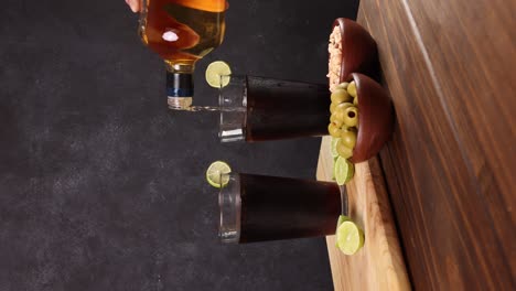 chilean piscola drink typical summer cocktail of chile glass with ice wooden board lemons with selective focus, dark background, vertical video