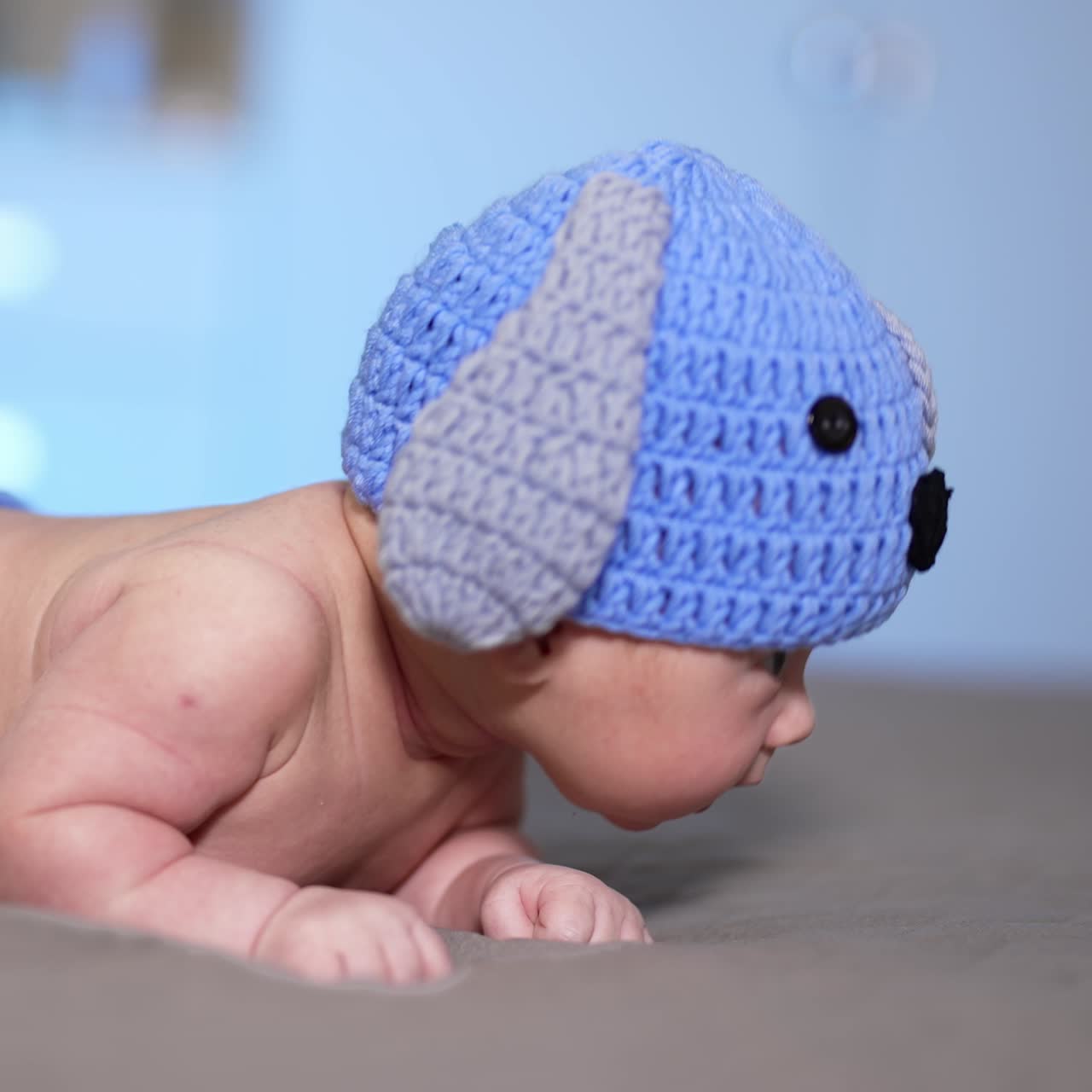 Little infant lying on his belly on the bed. Toddler just beginning to hold his head up. Small kid in a funny knitted hat with ears and diaper with tail