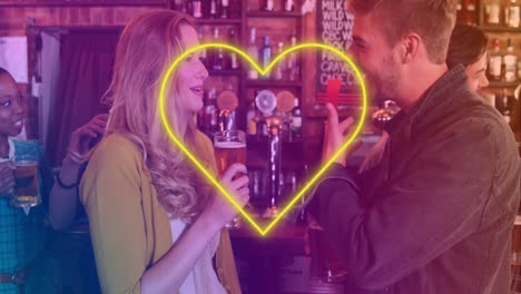 Animation-of-neon-yellow-heart-flickering-over-caucasian-couple-having-beer-in-bar