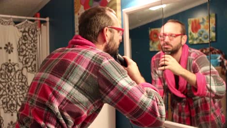 man trimming his beard in the bathroom mirror.
