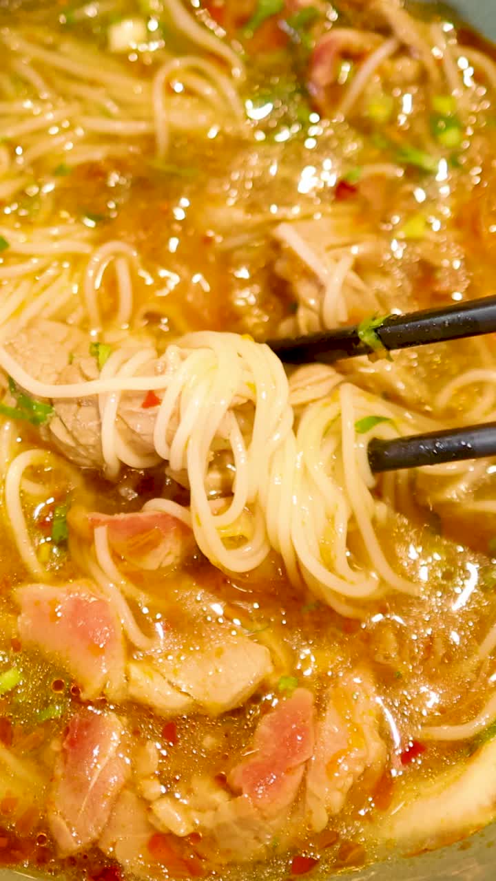 Bacchette sollevano noodles da una vivace zuppa vietnamita, mettendo in mostra un brodo ricco e ingredienti freschi in un ambiente caldo e accogliente.