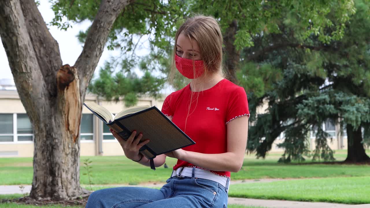 un joven estudiante universitario estadounidense estudia mientras se distancia socialmente y usa una máscara