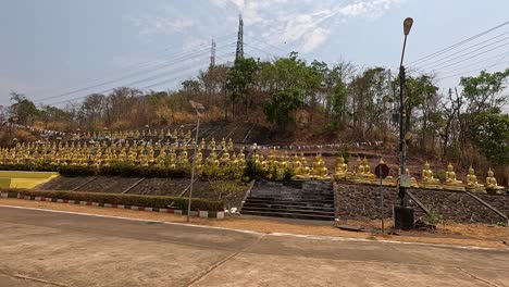 a smooth daytime camera pan reveals rows of golden buddhist statues and temple architecture along a quiet street in pakse, laos, under natural sunlight