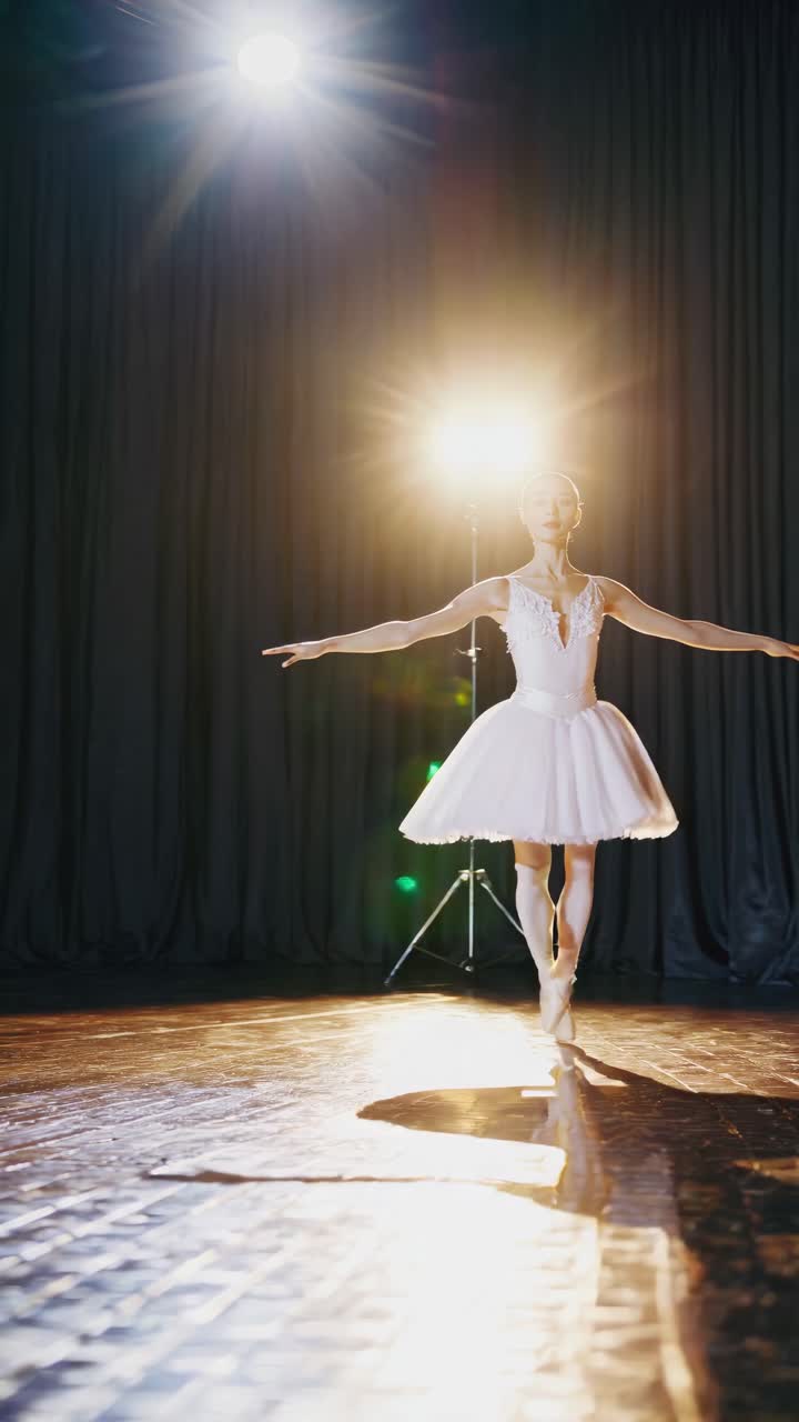 Una ballerina con un tutù bianco si esibisce sul palco, illuminata in controluce da un riflettore.