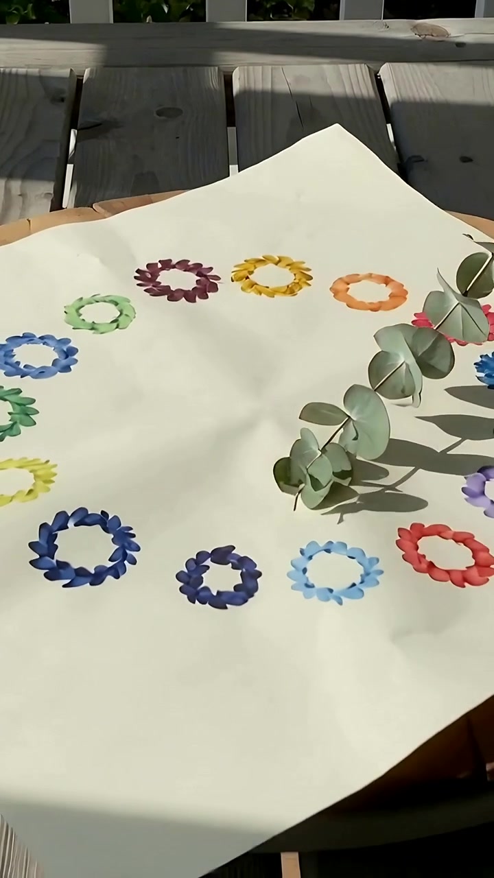 Vertical video: Breeze nudging eucalyptus stem across cream sheet on deck, shading painted wreaths