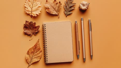 Autumn-Leaves-With-Notebook-And-Pens-On-Orange-Background