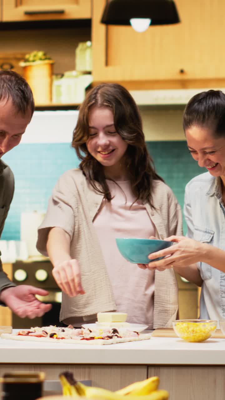 Vertical Video Parents and tween girl laughing while sprinkling mozzarella on pizza