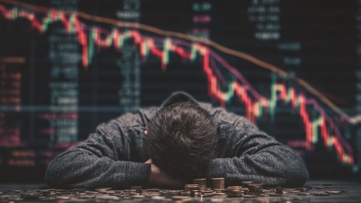 Una cupa riflessione sulla disperazione finanziaria: una persona si appoggia con la testa su una scrivania circondata da monete, illustrando il costo emotivo della volatilità del mercato e dello stress economico
