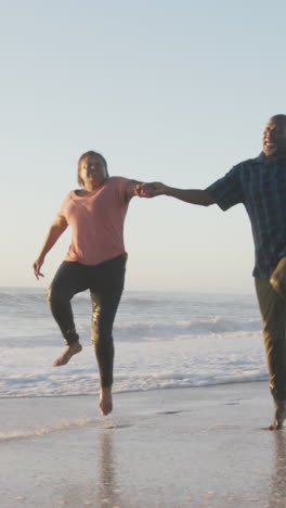 smiling senior african american couple holding hands and running on sunny beach