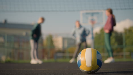 volleyball placed on the ground in outdoor sport arena with yellow marking visible, athlete in the background engaged in fitness exercise, with a focus on the volleyball and movement