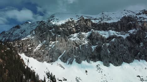 wide panorama panning flight at a glacier rock snow mountain top near bavaria elmau castle in the bavarian austrian alps on a sunny day along trees and forest in nature with avalanches going down