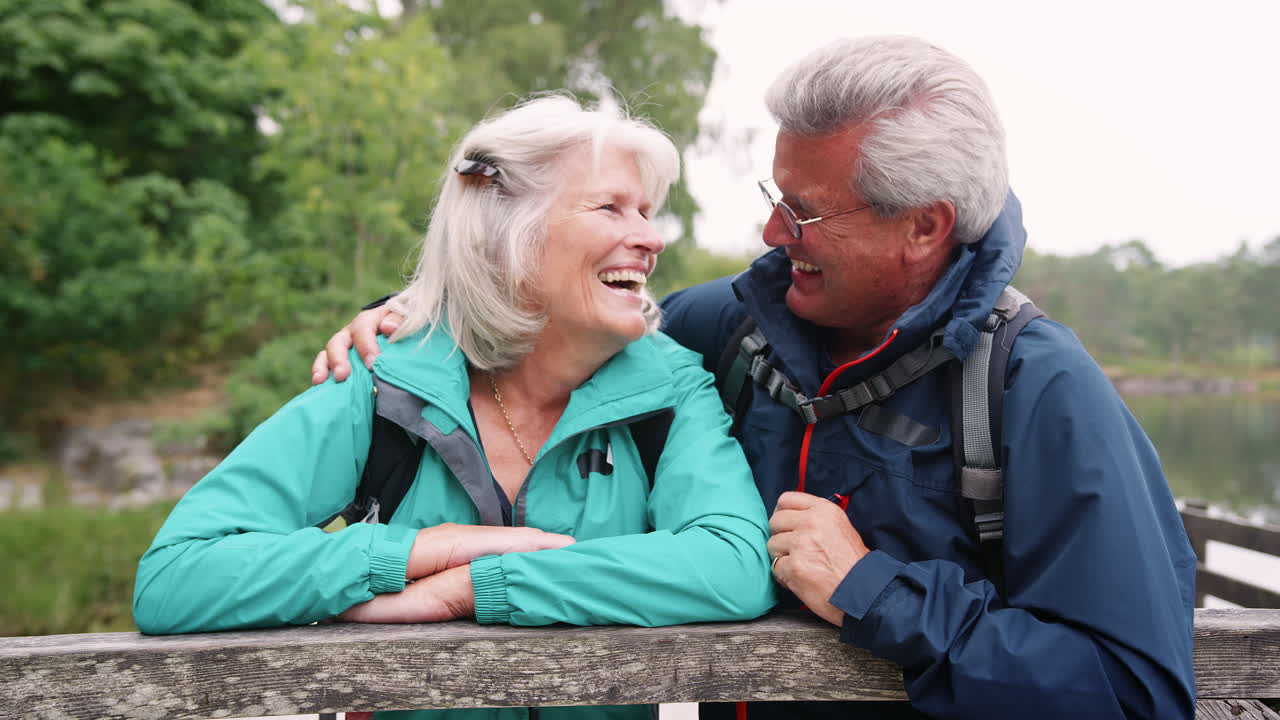 Happy senior couple leaning on a wooden fence laughing to camera, close up, Lake District, UK