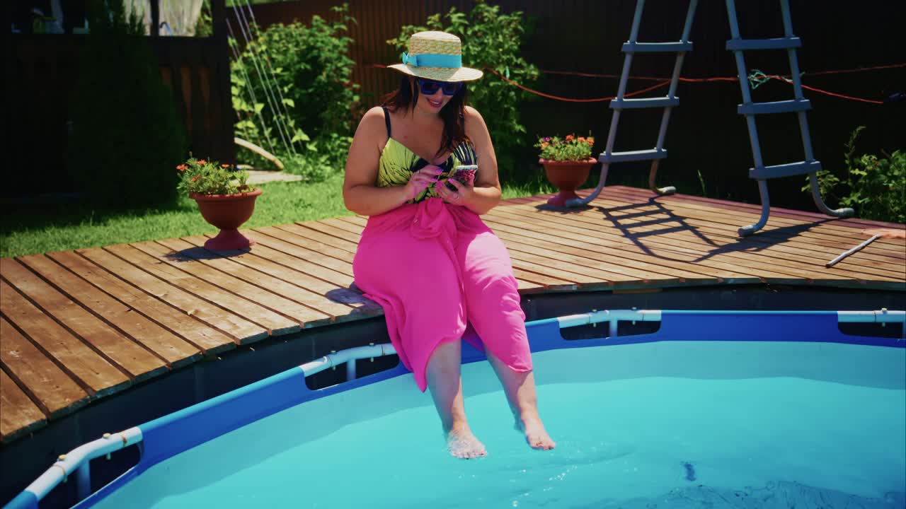 Woman relaxing by swimming pool, wearing sun hat and pink skirt, enjoying summer leisure time