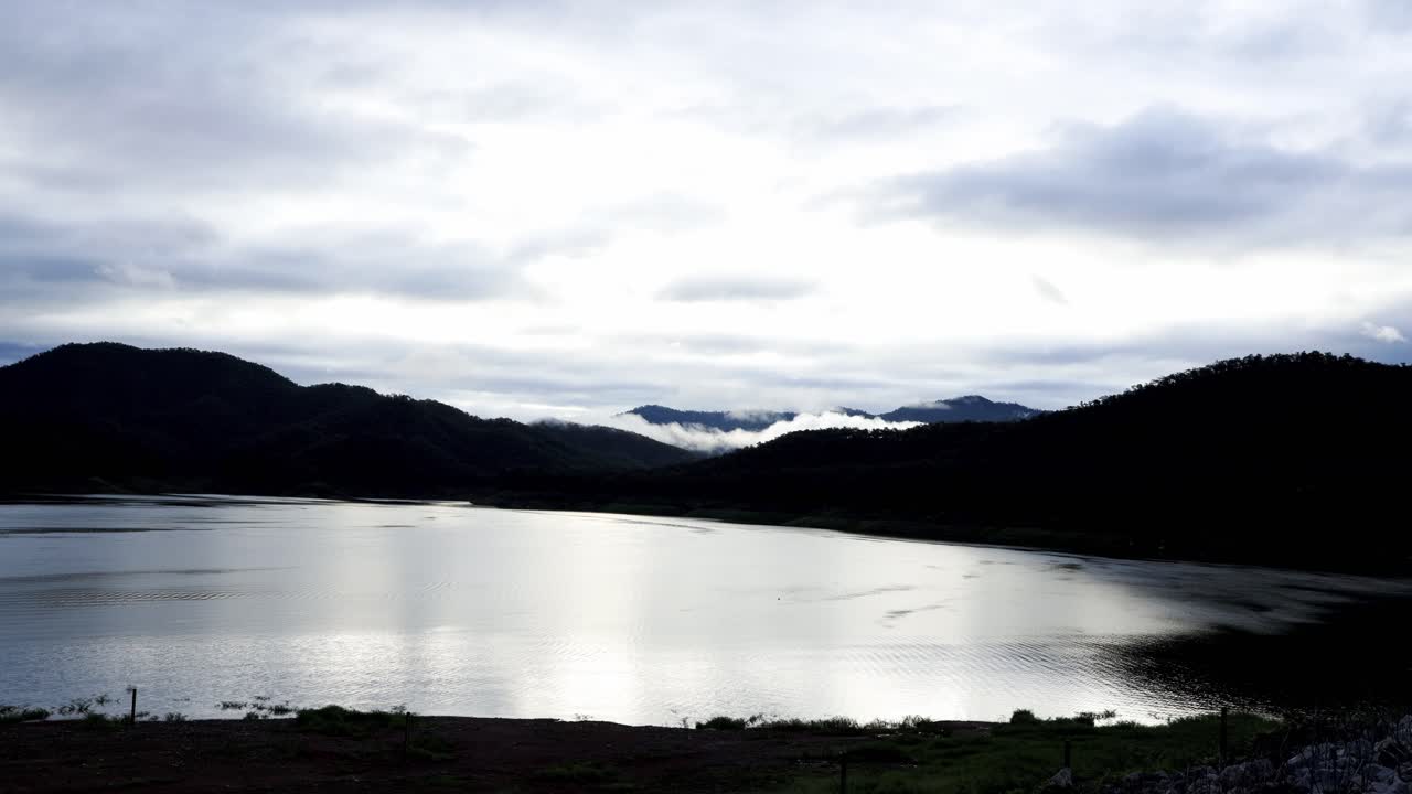 일출의 광선으로 아침에 산 범위와 호수에 뇌우 후 흐린 하늘의 시간 경과