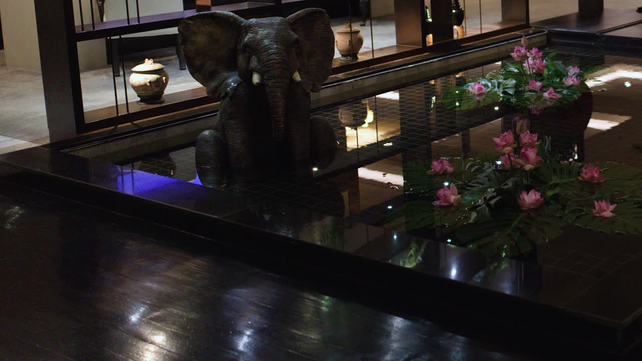 Slow pan of indoor elephant statue, lotus flowers, and fountain in elegant Bangkok hotel lobby