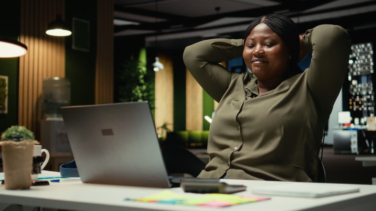 Black company worker reclining in a chair and relaxing at midnight