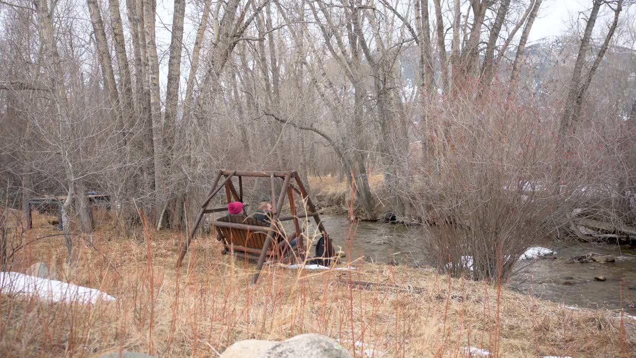 겨울 에 강 앞 에 나무 로 된 흔들리는 벤치 에 앉아 있는 부부, 정적