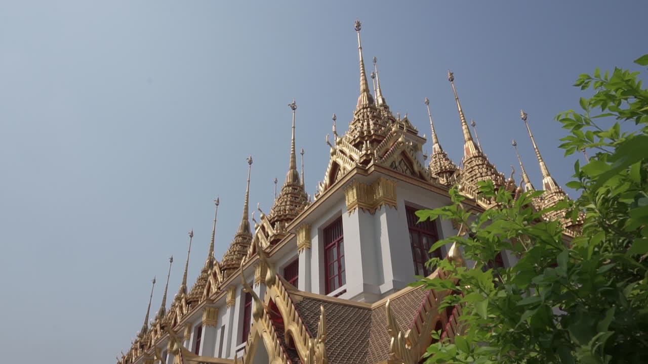 Dolly in by some green plants to reveal an important big white and golden buddhist temple or castle in the city of Bangkok in Thailand
