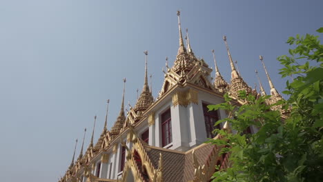 dolly in by some green plants to reveal an important big white and golden buddhist temple or castle in the city of bangkok in thailand