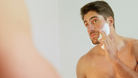 Young-man-looking-into-mirror-applying-shaving-foam-on-his-face-4K-4k