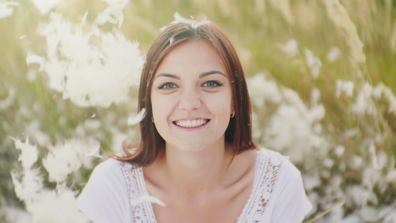 젊은 여성의 초상화는 그녀의 앞과 아래로 깃털 아래로 카메라를 본다