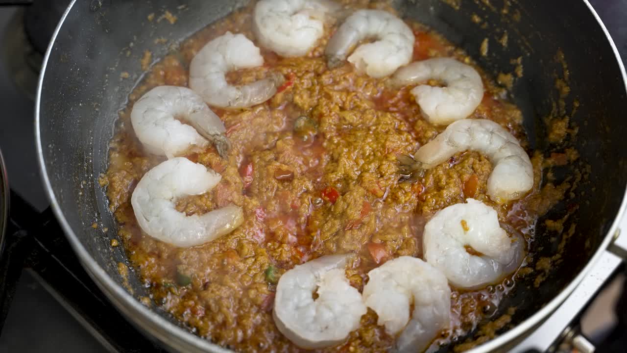 una persona agrega delicadamente camarones a una salsa caliente y burbujeante en un plato, capturada en cámara lenta, mostrando la experiencia culinaria y el placer de comer