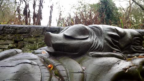 Log-carved-wooden-piglet-sitting-in-wet-autumn-woodland-nature-reserve-forest-dolly-right