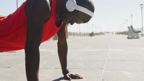 Focused-african-american-man-doing-press-ups,-exercising-outdoors-by-the-seaside