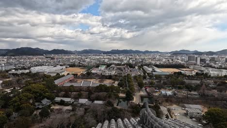 captured from the top of himeji castle, this panoramic view showcases the blend of traditional tiled rooftops, tree-lined avenues, and the expansive city of himeji under a dramatic sky.