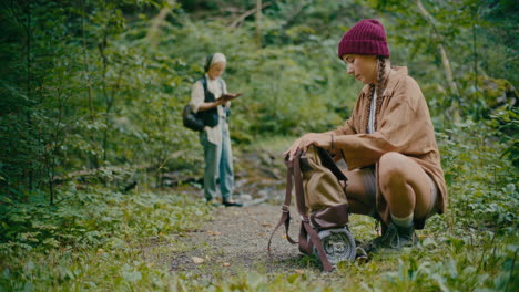 woman packing backpack while crouching near plants