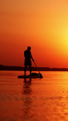 bright setting sun reflecting in the river. black male silhouette sup boarding on the river at sunset. vertical video