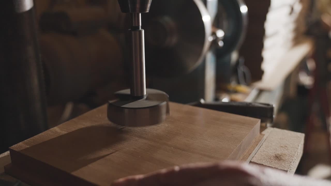 Wood drill going into board cutting hole, sawdust shavings flying away, slow motion