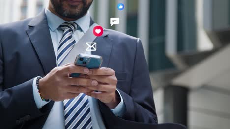 close up de un hombre de negocios de pie fuera de las oficinas de la ciudad mirando un teléfono móvil con emojis de gráficos de movimiento que muestran múltiples mensajes y notificaciones de redes sociales