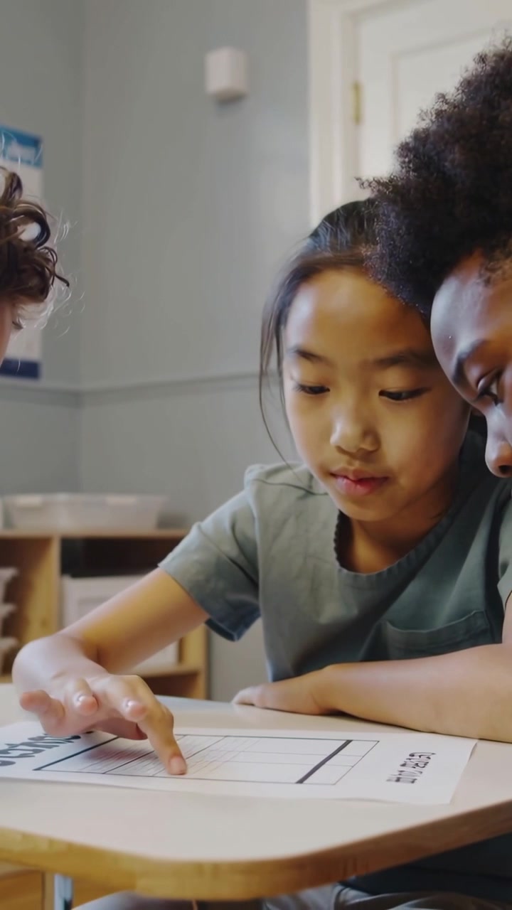 Vertical video: Pointing central girl in muted tee guiding peers at school desk solving grid