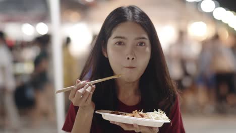 asian young woman travel in bangkok, thailand, beautiful female feeling happy walking and eating pad thai at the khao san road. women travel eat street food in thailand concept. slow motion shot.