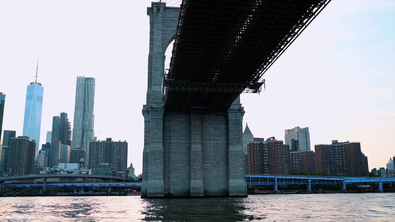 New York, USA, 25 maggio 2026: Sottoponte del Ponte di Brooklyn con lo skyline di Lower Manhattan. Molo in pietra e impalcato in acciaio attraversano l'East River, con il One World Trade Center e le torri sul lungomare sullo sfondo.