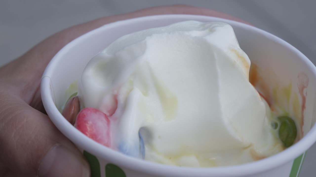 Fresh frozen yogurt in a cup, topped with a spoonful of creamy goodness and vibrant toppings