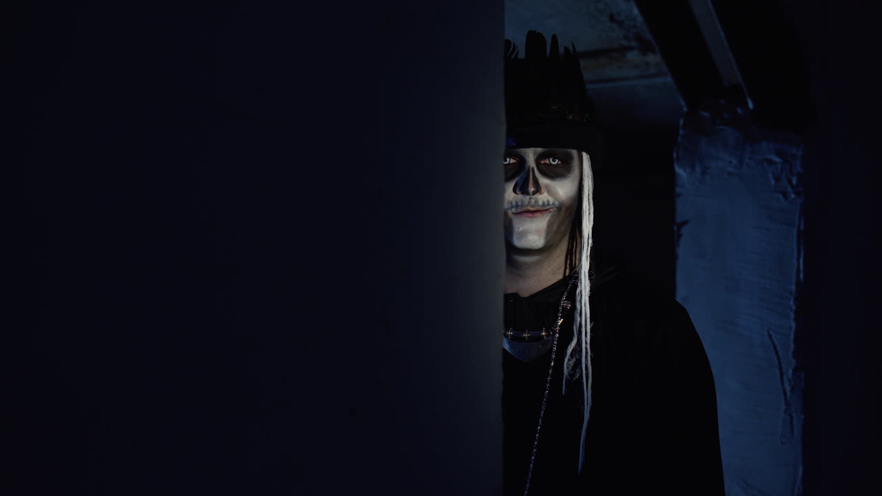 un hombre siniestro con maquillaje de esqueleto de halloween aparece lentamente desde un rincón oscuro con una sonrisa aterradora.