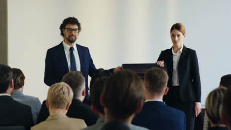 caucasian businesswoman and businessman on a podium in front of the auditory and presenting a project at a conference