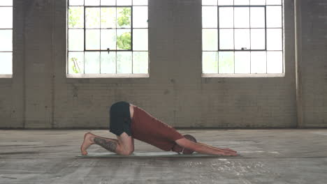 man in an industrial warehouse practicing yoga doing a puppy pose.
