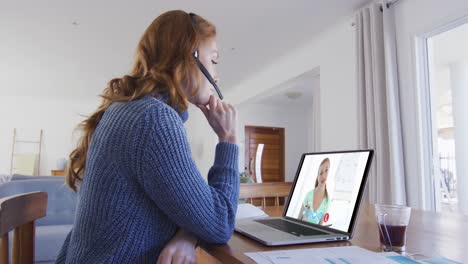 mujer caucásica usando portátil y auriculares de teléfono en videollamada con una colega