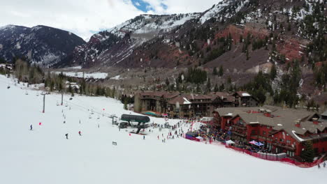 skiing resort building complex with cable lift and happy people ski, aerial drone view during snowfall