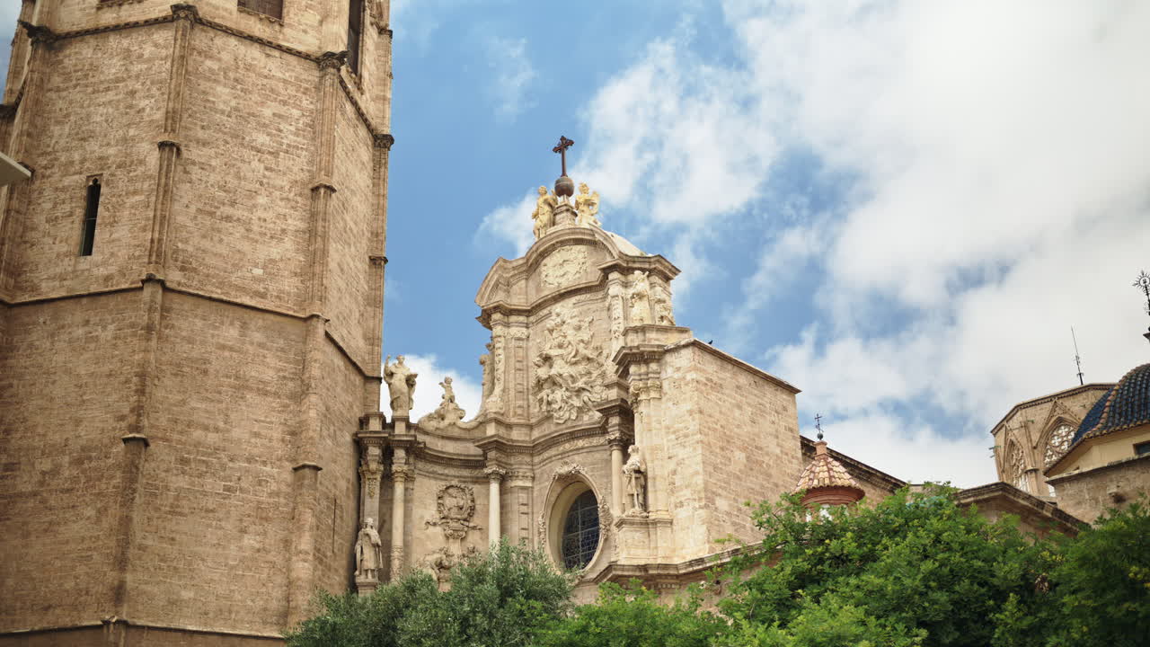 Low angle view of the Baroque main portal and adjacent bell tower of Valencia Cathedral, framed against a bright blue sky in Valencia, Spain