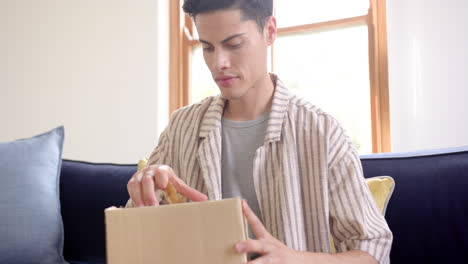 Excited-biracial-man-opening-delivery-in-cardboard-box,-slow-motion