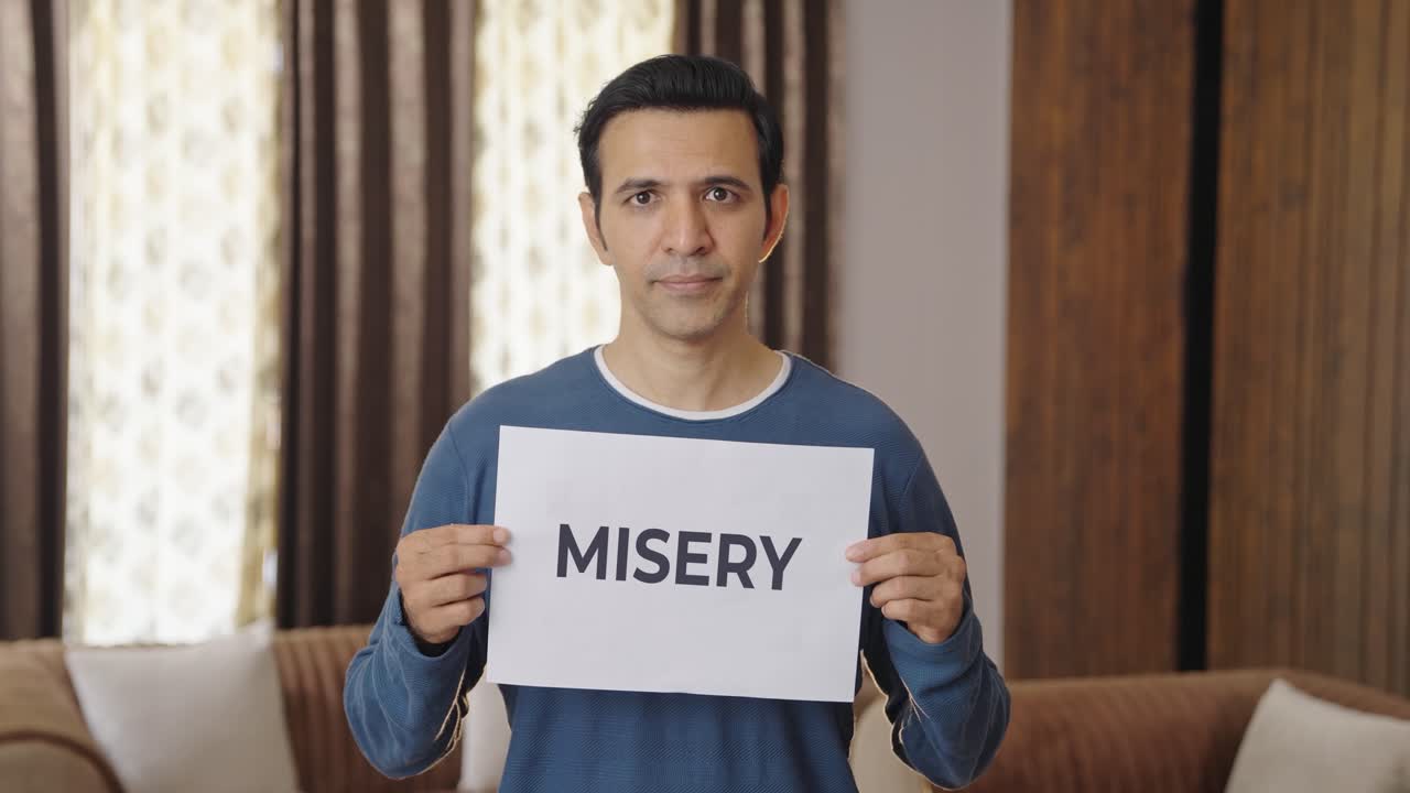Sad Indian man holding MISERY banner