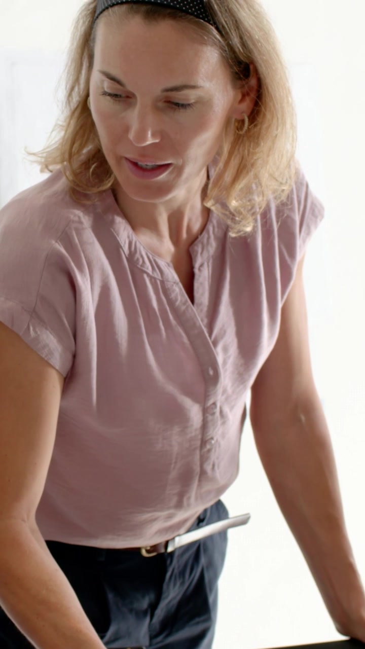 Vertical video: Noticing yellow disc, woman reaching over table, placing item, mauve top dark pants