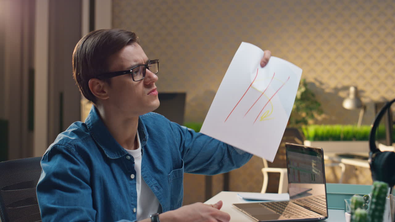 Uomo oberato di lavoro che disegna uno schizzo mostrandolo a un collega, primo piano. Colleghi che lavorano fino a tardi.