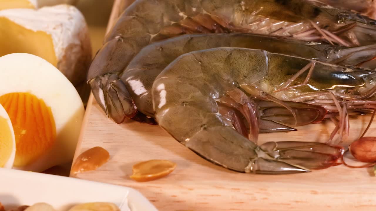 A selection of protein-rich foods including eggs, shrimp, chicken, beef, and nuts displayed on a wooden surface.