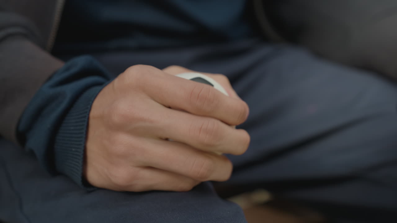closeup hand holding small soccer ball showing slow therapeutic squeeze for grip recovery, seated man in navy sweatshirt performing repetitive finger and palm exercises, focused motion on tendons